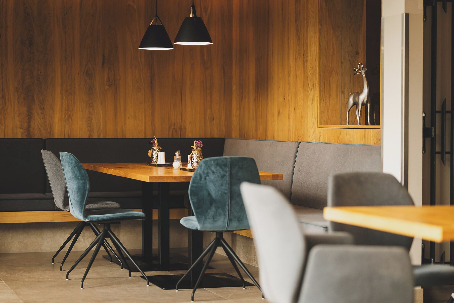 Un comedor moderno con paneles de madera, lámparas colgantes negras y una mesa de madera con sillas.