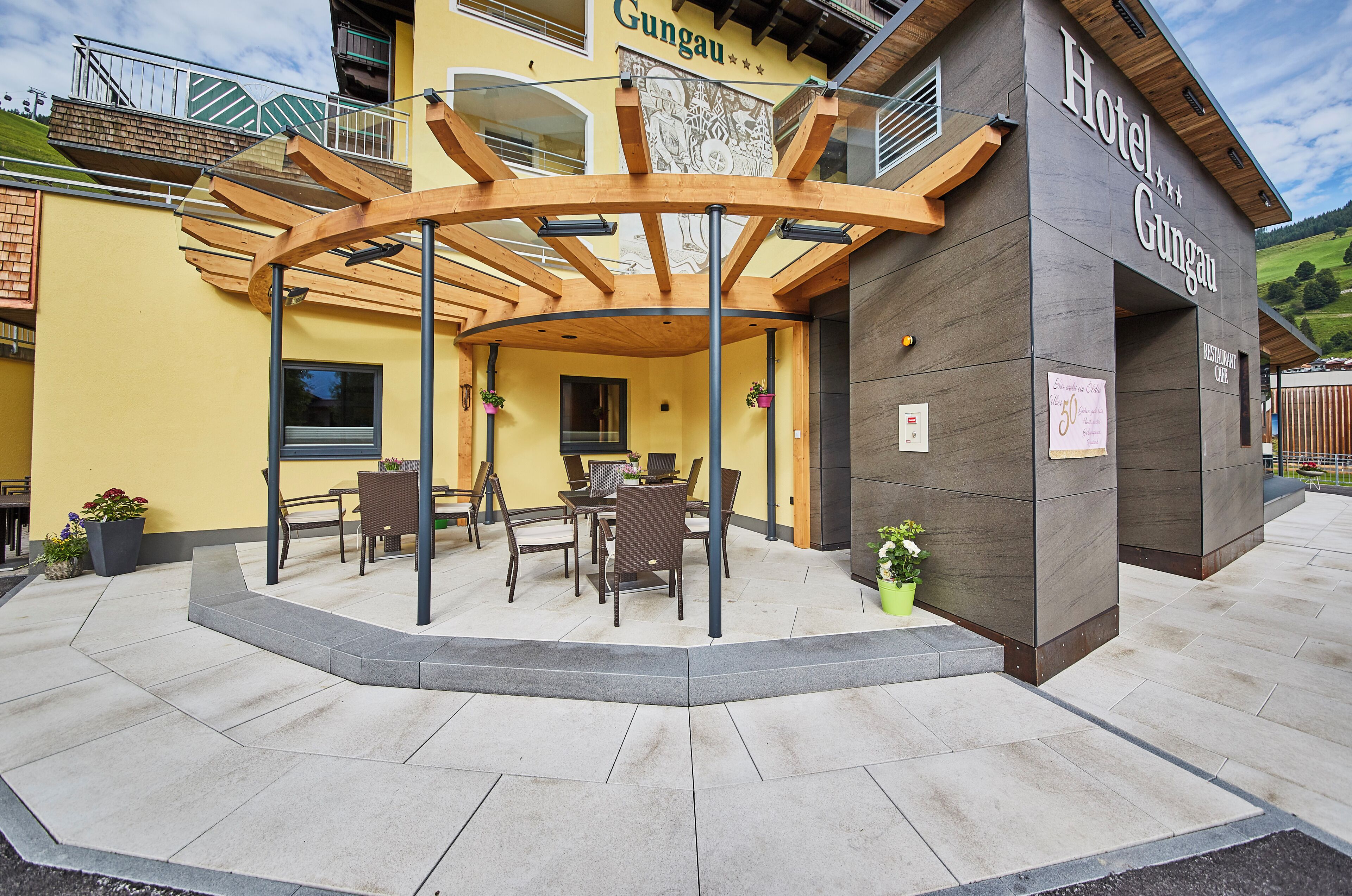 A hotel with a covered outdoor seating area, a restaurant cafe, and a mountain view.
