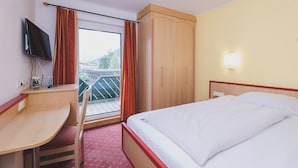 Habitación de hotel con cama, escritorio, televisor, armario y balcón con vistas.