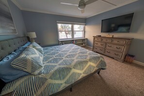 Ein Schlafzimmer mit Bett, Schminktisch, Fernseher und Fenster mit Blick auf den Strand.