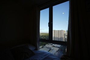 Ein Schlafzimmer mit einem großen Fenster mit Blick auf eine Stadtlandschaft und den Mond.