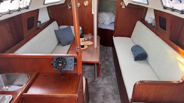 A compact boat interior with a kitchenette, two seating areas, and a small bed.