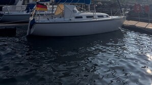 A sailboat docked at a marina with other boats, a clear sky, and a calm water surface.
