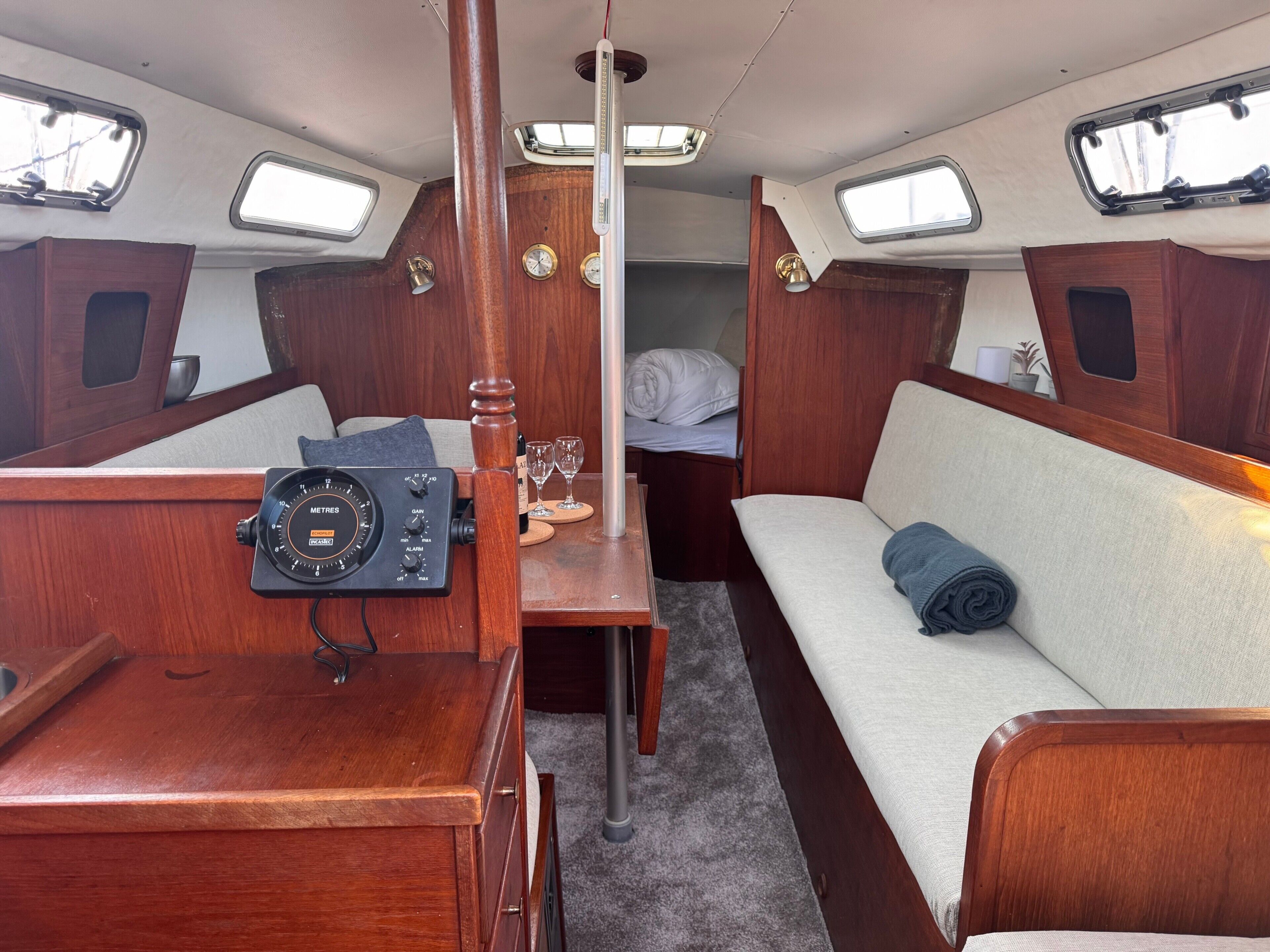 Een hutje met een bedieningspaneel, een bed met een opgerolde deken, en een kleine tafel met glazen.