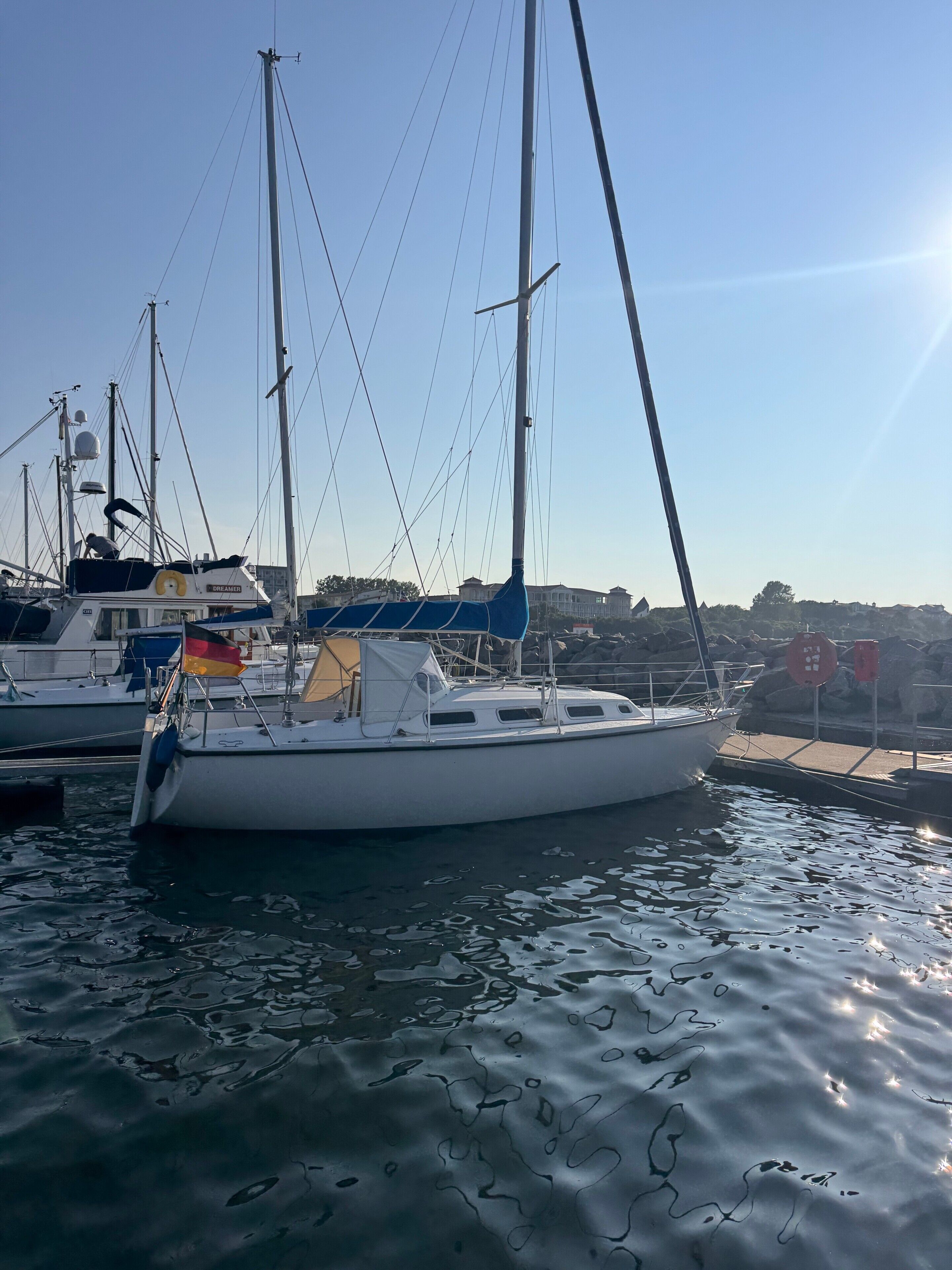 Een zeilboot afgemeerd in een jachthaven, met andere boten, rustig water en een heldere lucht.
