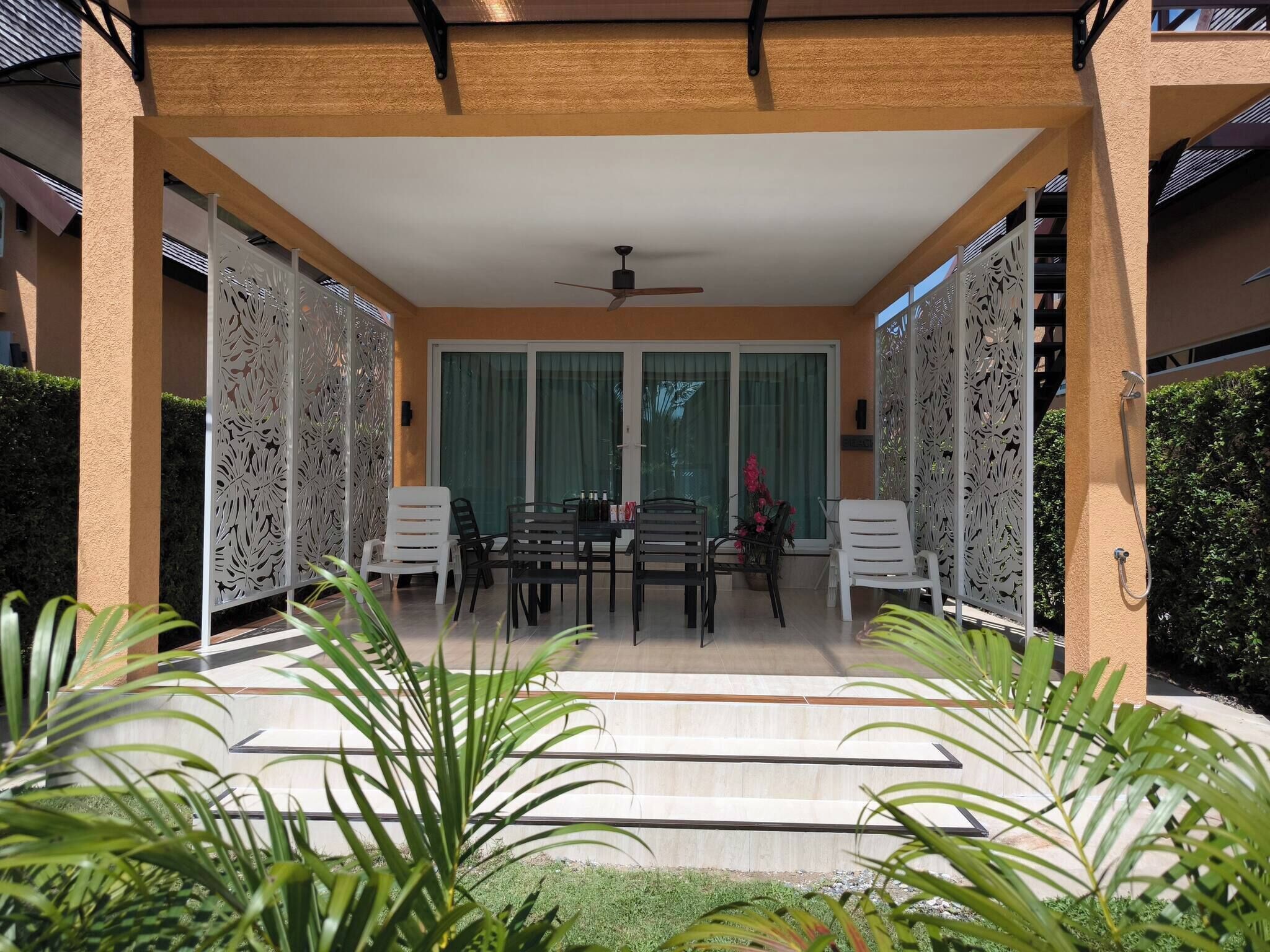 Um pátio externo com mesa e cadeiras, cercado por painéis decorativos e plantas em vasos.