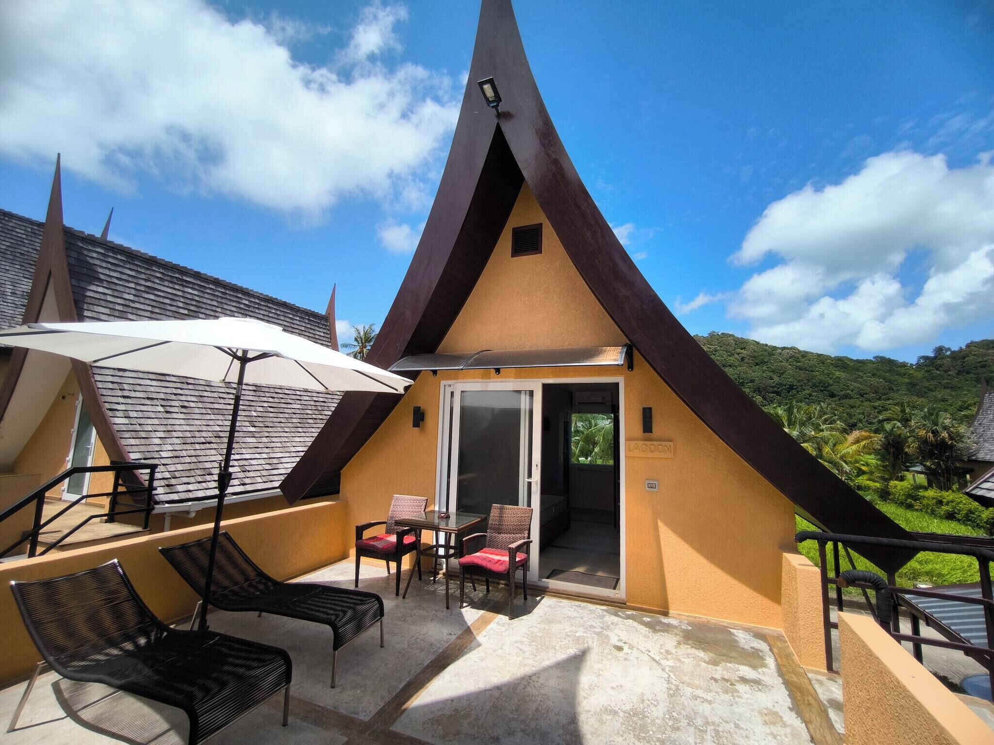 Un edificio con tetto a punta e patio, con sedie, tavolo e vista su un paesaggio lussureggiante.