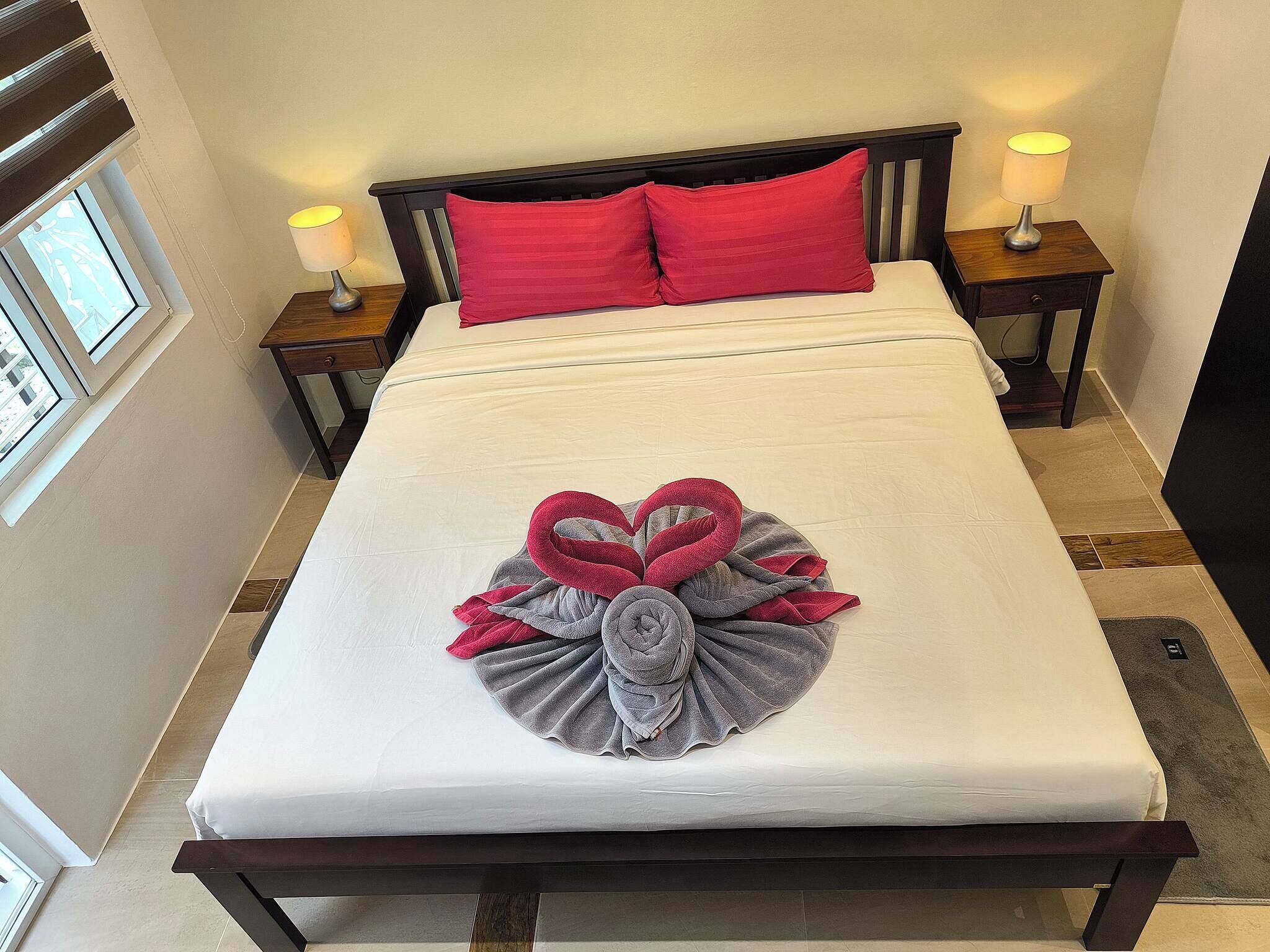 Una cama bien hecha con una decoración de toallas, dos lámparas de noche y una ventana con persianas.