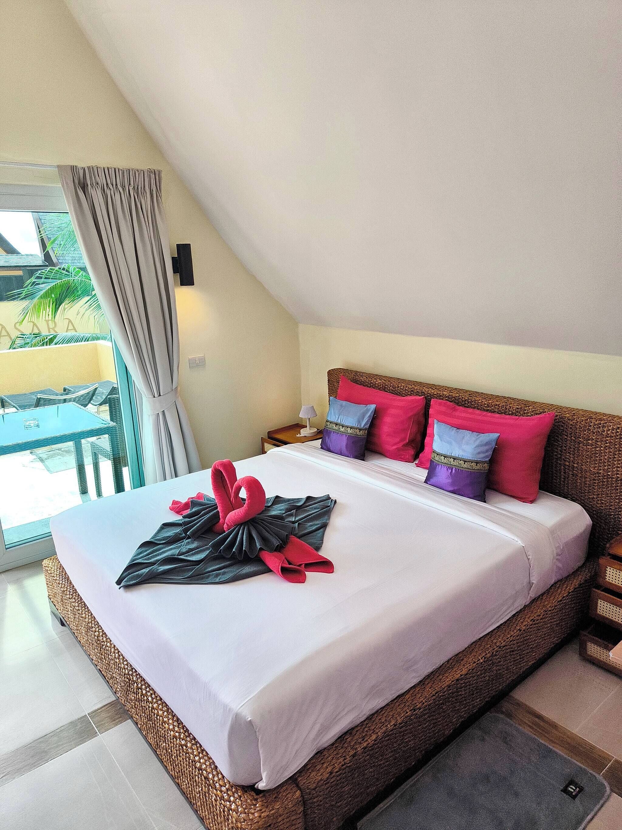 Quarto de hotel com cama, almofadas, mesa de cabeceira, abajur e vista para o exterior.