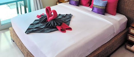 A hotel room with a bed, pillows, a nightstand, a lamp, and a view of the outside.