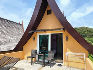 A triangular-shaped building with a glass door entrance, outdoor seating area with chairs, and a metal drying rack.