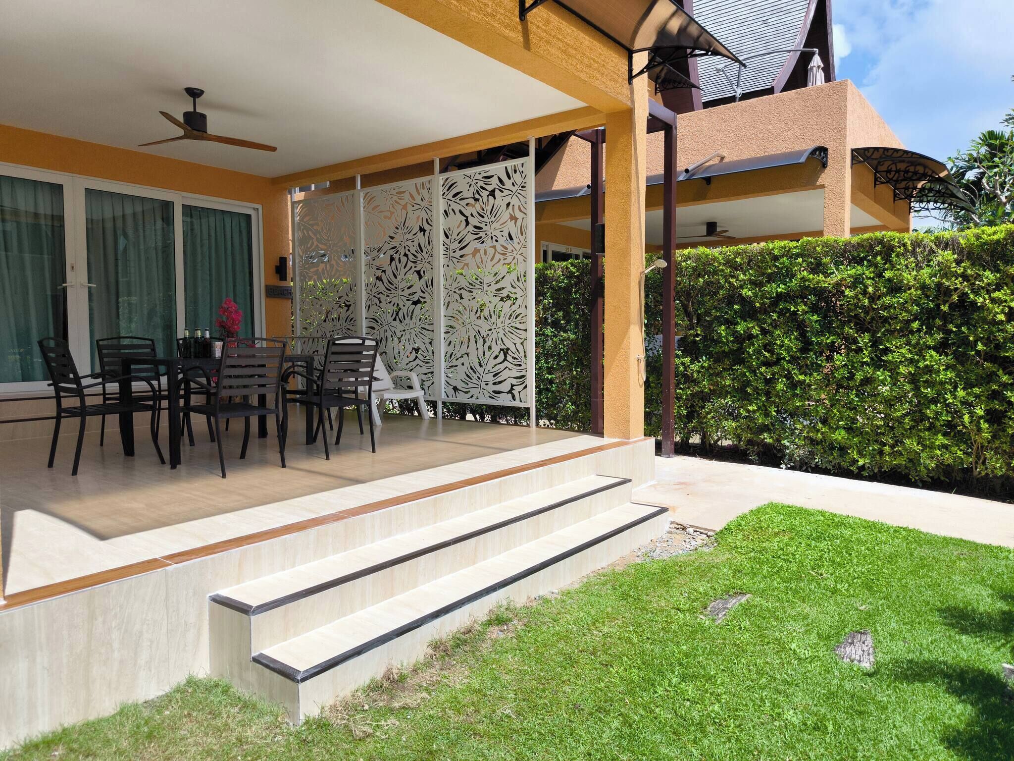 A covered outdoor seating area with a table and chairs, a decorative screen, and a staircase leading to a covered patio.