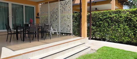A covered outdoor seating area with a table and chairs, a decorative screen, and a staircase leading to a covered patio.