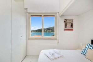 A bedroom with a bed, a window with a view of the sea, and a small artwork on the wall. - [Portoseaview] Terrace+A/C (Portovenere)