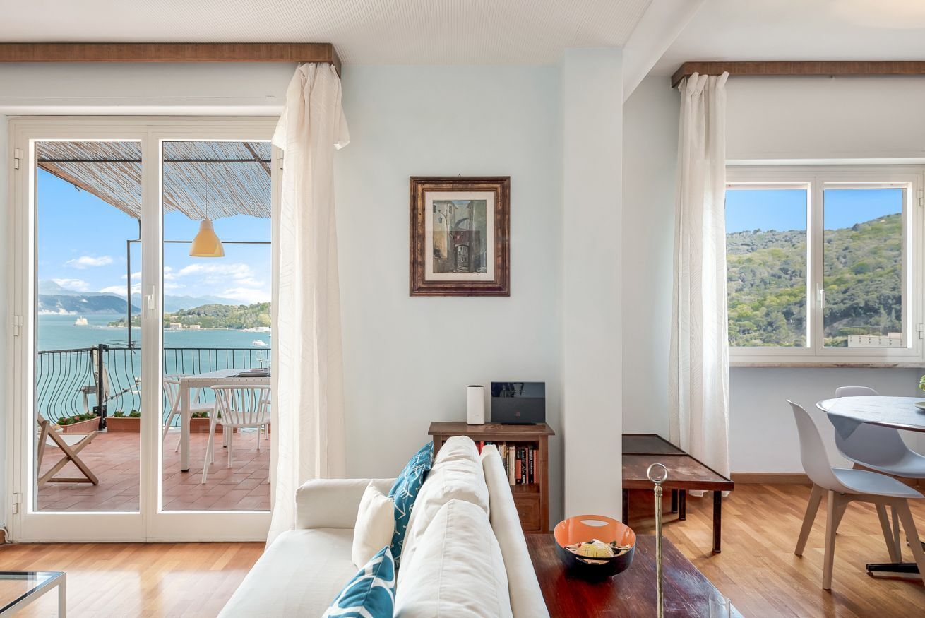 Una sala de estar con sofá, una mesa de comedor y vista al mar por un ventanal corredero.