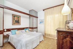 A hotel room with a double bed, wooden headboard, a nightstand, a desk, and a large window with curtains. - [Portoseaview] Terrace+A/C (Portovenere)
