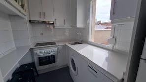 A compact kitchen with white cabinets, a built-in oven, a washing machine, and a window providing natural light. - Ideal Accommodations in Madrid – Calle Cicerón with a Terrace (MADRID centro)