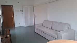 A room with a sofa, a wooden table with a keyboard, a TV, and a wardrobe. - Ideal Accommodations in Madrid – Calle Cicerón with a Terrace (MADRID centro)