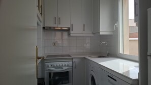 A compact kitchen with a stove, oven, and washing machine. - Ideal Accommodations in Madrid – Calle Cicerón with a Terrace (MADRID centro)