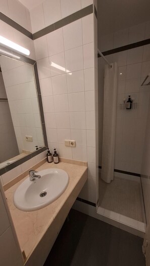 Ein Badezimmer mit einem weißen Waschbecken, einem Spiegel und einer Duschkabine.