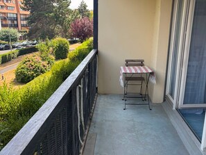 A balcony with a small table and chair, a view of a road and greenery, and a building in the background. - Charming apartment near the beach - 2 guests (Villers-sur-Mer)