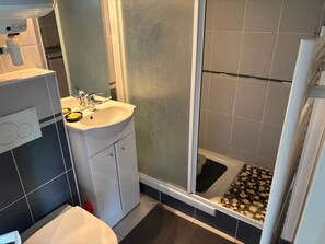 A bathroom with a white sink, a mirror, and a shower area with a black and white tiled floor. - Charming apartment near the beach - 2 guests (Villers-sur-Mer)