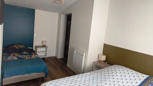 A bedroom with two beds, a bedside table with a lamp, a radiator, and a hanging light fixture.