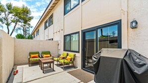 An outdoor patio with a barbecue grill, two green cushioned chairs, a wooden table, and a covered grill area. - 25% Off Sept 10-13 Perfect 4 Families Pool, Tennis (Palm Springs)