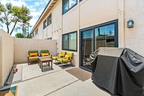 An outdoor patio with a barbecue grill, two green cushioned chairs, a wooden table, and a covered grill area. - 25% Off Sept 10-13 Perfect 4 Families Pool, Tennis (Palm Springs)