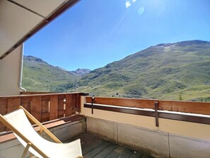 Ein Balkon mit Holzboden und einem weißen Stuhl, mit Blick auf eine Berglandschaft unter blauem Himmel.