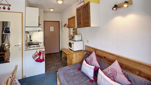 Quarto compacto com uma cama, uma cozinha compacta e um armário de madeira.