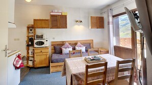 Quarto compacto com cama, uma mesinha, uma cadeira, micro-ondas e armários de madeira.