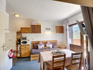 Ein kleines Zimmer mit einem Bett, einem Tisch, einem Stuhl, einer Mikrowelle und Holzschränken.