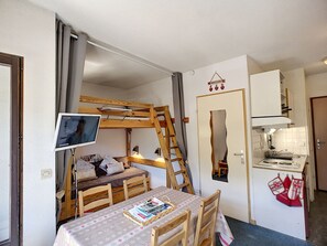 Ein kompakter Raum mit Etagenbett, Schreibtisch, Computerbildschirm, kleiner Küchenzeile und Essbereich mit Tisch und Stühlen.