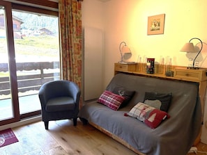 A cozy room with a sofa, a chair, a wooden shelf with decorative items, and a window with curtains. - Apartment with pets allowed - 4 guests at the foot of the slopes (Arêches-Beaufort)