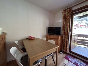 Ein Essbereich mit Tisch, Stühlen, einem Fernseher und Blick auf eine verschneite Landschaft durch ein Fenster.