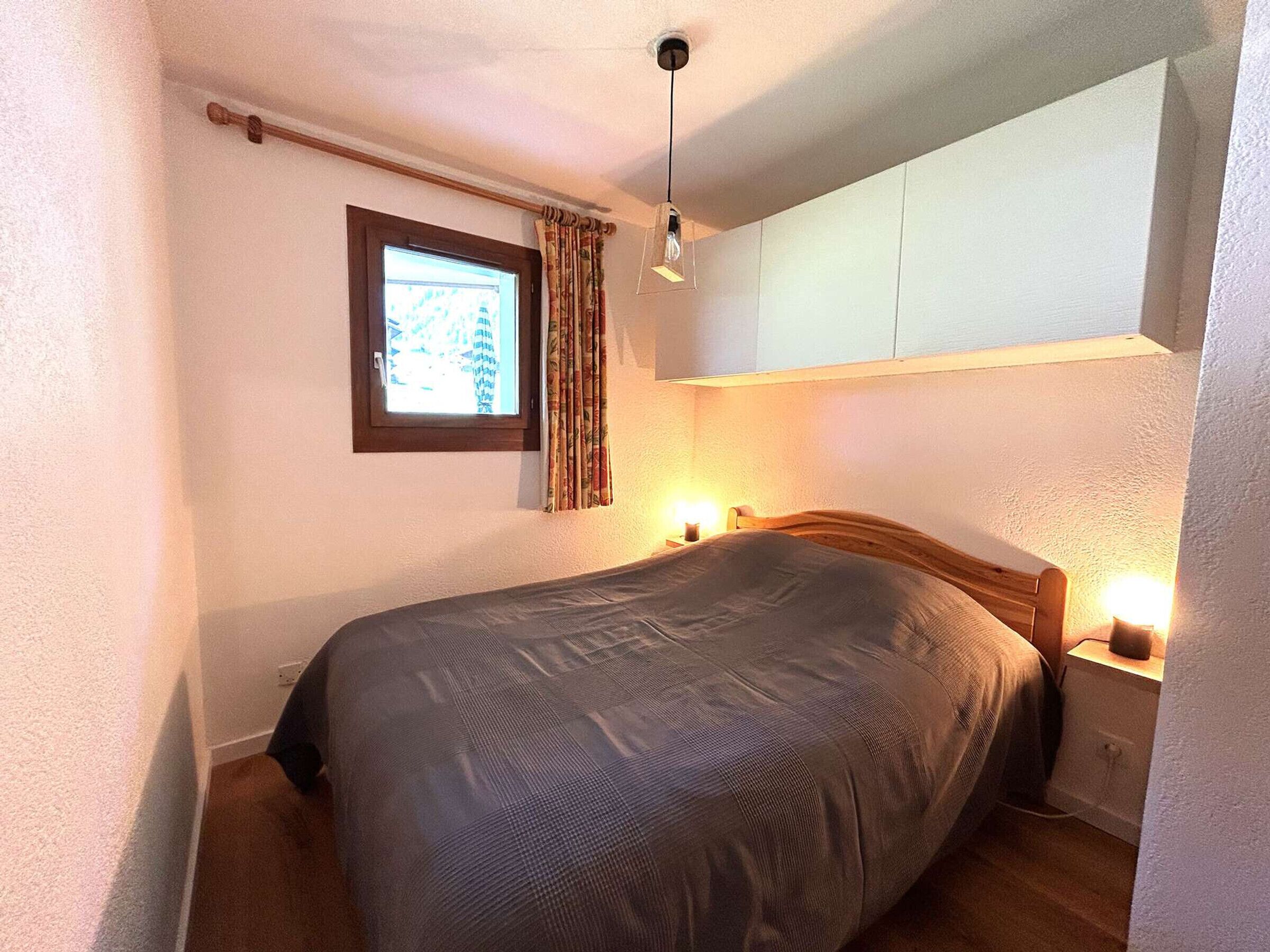 Una cama individual con cabecera, una mesita de noche con lámpara, una ventana con cortinas y una lámpara en el techo.