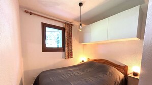 Una cama individual con cabecera, una mesita de noche con lámpara, una ventana con cortinas y una lámpara en el techo.