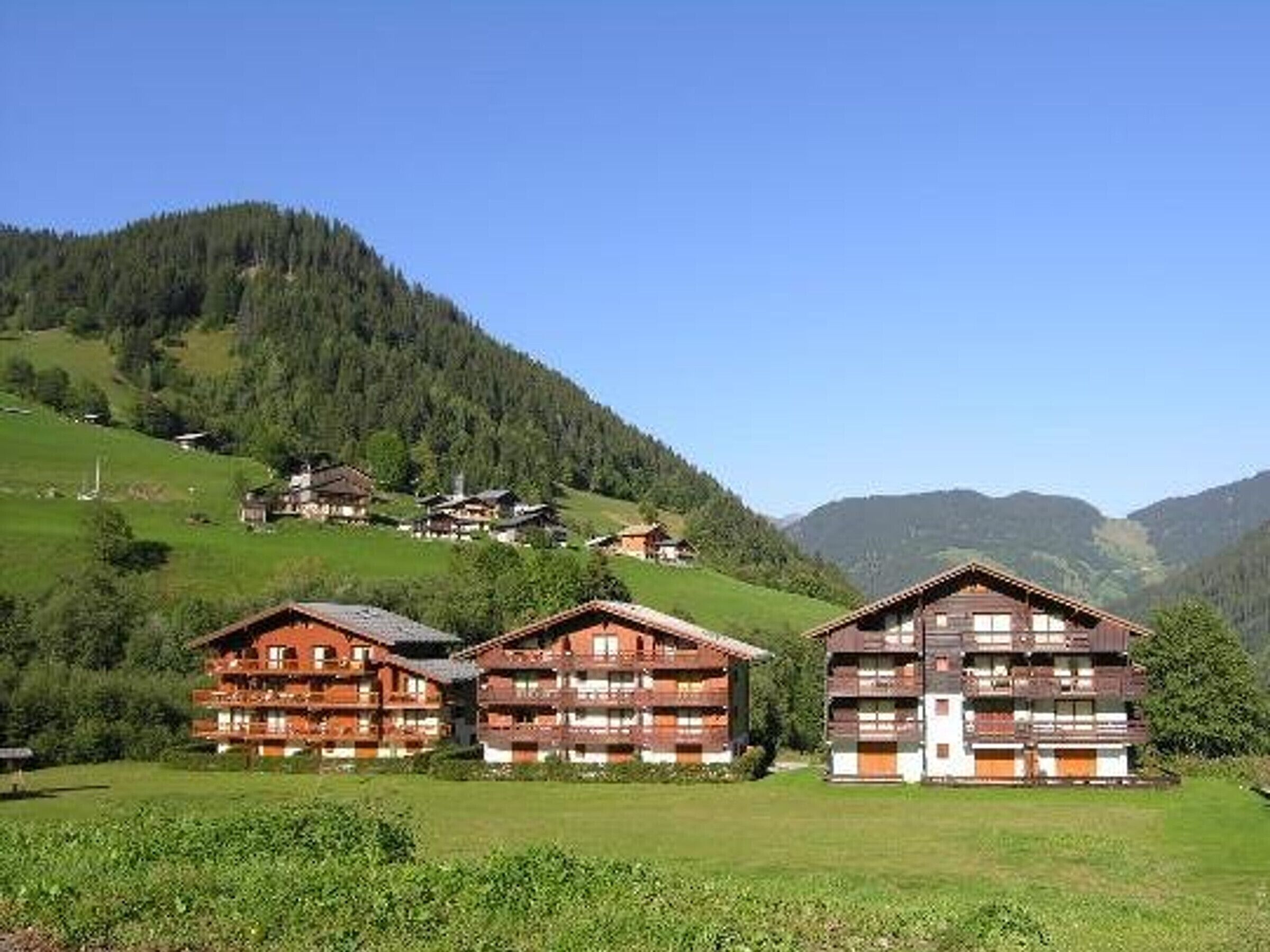 A mountain lodge with multiple wooden buildings, surrounded by lush greenery and hills.