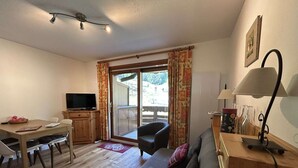 Una sala amueblada con un sofá, una televisión, una mesa de comedor y un gran ventanal corredizo que da a un espacio exterior.
