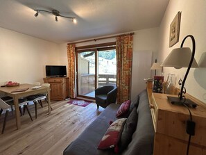 Ein möbliertes Wohnzimmer mit einer Couch, einem Fernseher, einem Esstisch und einer Schiebetür zu einem Außenbereich.