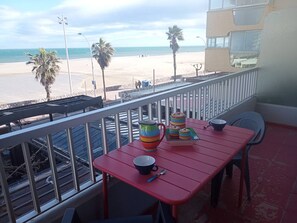 A balcony with a red table, a black mug, and a colorful striped mug on it. - Spacious apartment sea view - 4 guests (Canet-Plage)
