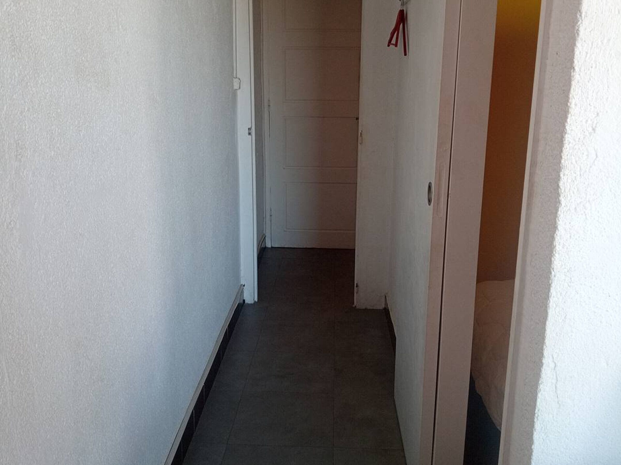 A narrow hallway with a door at the end, a light switch on the wall, and a red object hanging on the door frame.