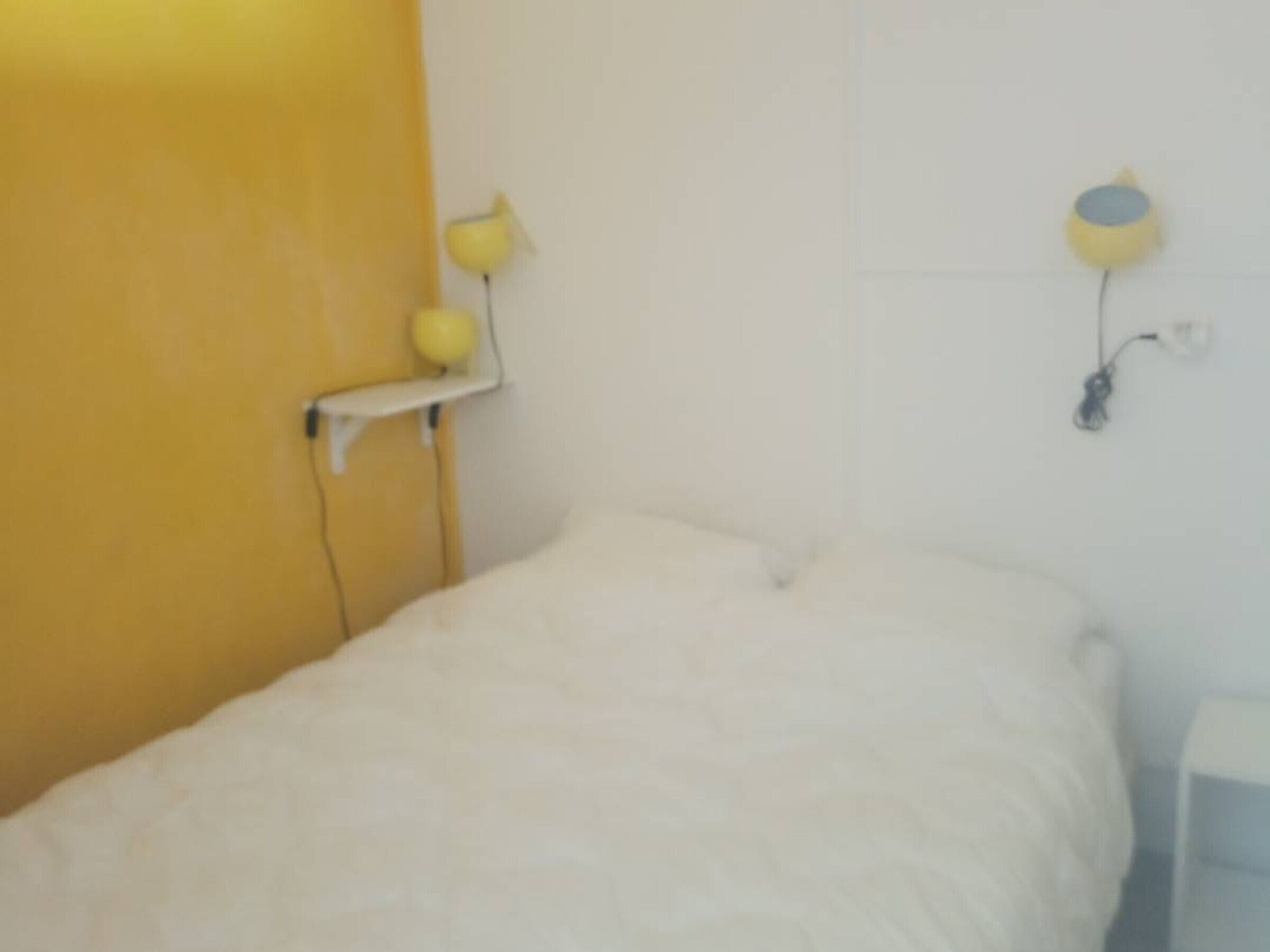 A bed with a white mattress and a yellow wall.
