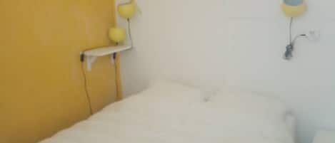 A bed with a white mattress and a yellow wall.