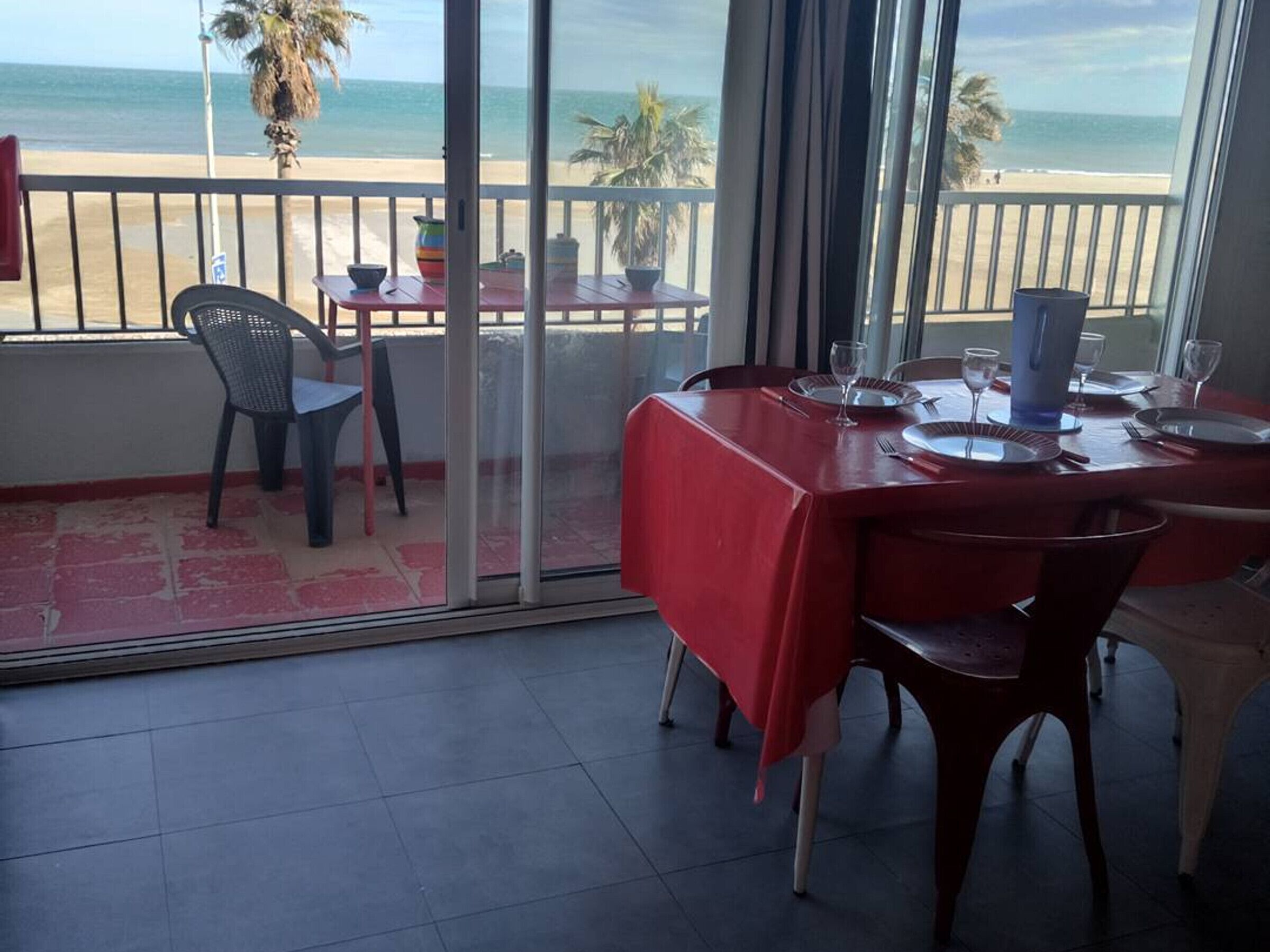 A dining area with a red table, chairs, and a view of the beach.