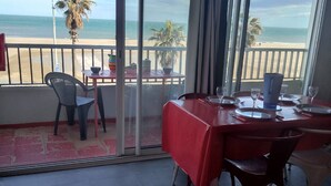 Un comedor con una mesa roja, sillas y vista a la playa.