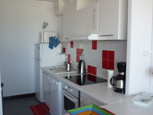 Cocina compacta con gabinetes blancos, un lavamanos de acero inoxidable, cafetera y escurreplatos.