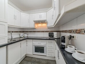 A compact kitchen with white cabinets, a black countertop, a microwave, a coffee maker, and two cups on the counter. - Modern Studio in Costa Adeje with Spacious Terrace (Costa Adeje)