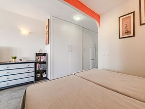 A bedroom with a bed, a wardrobe, a bookshelf, and a small plant.